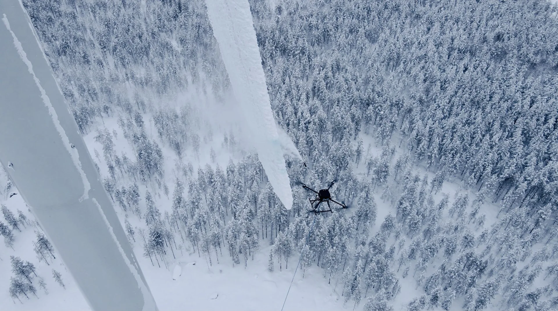 Drone ved en isdækket vindmøllevinge over snedækket skov under afisning