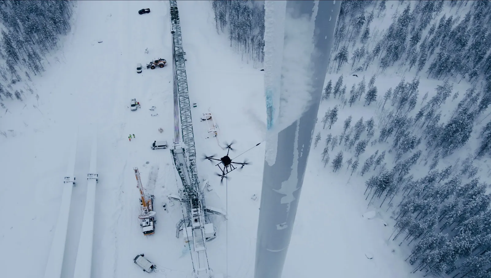 Drone og kran ved en vindmølle under afisning i snevejr