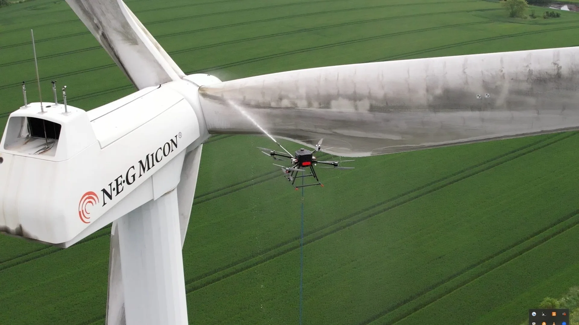 Drone spraying water onto a wind turbine blade during cleaning above green fields