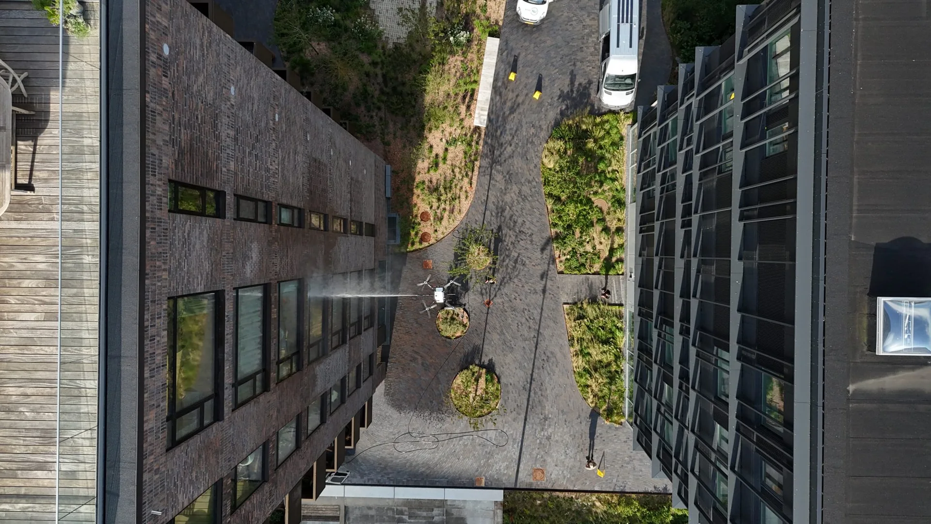 Facadevask med drone mellem to bygninger, set ovenfra med slange og arbejdsbiler