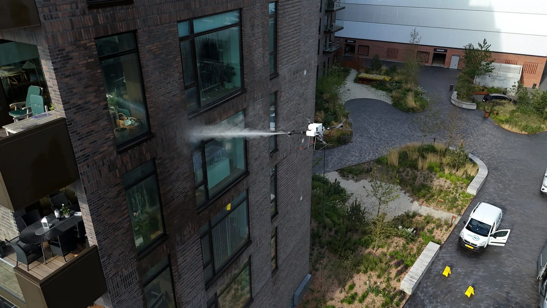 Drone vasker vinduer og murstensfacade med en vandstråle, set fra siden