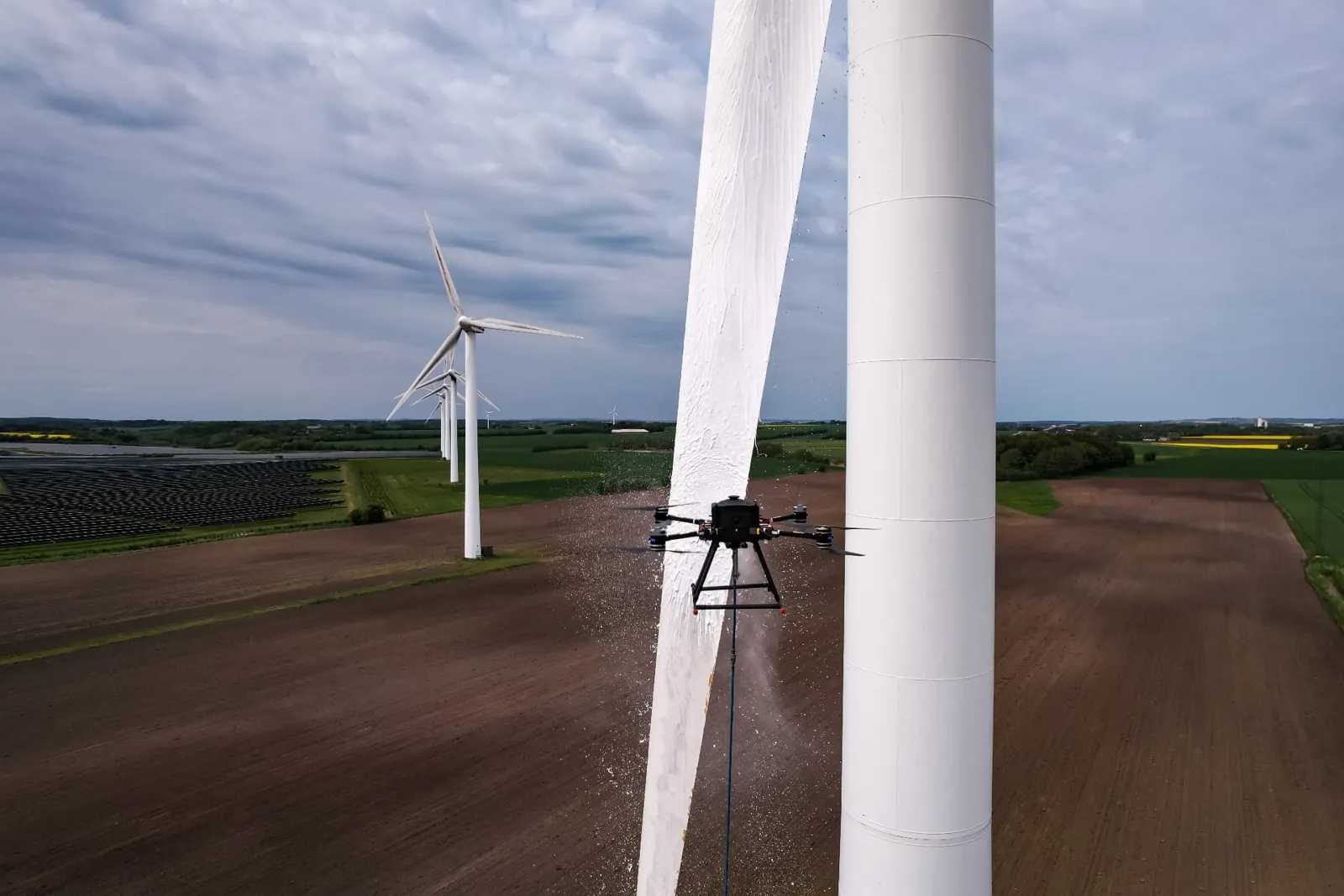 Drone tæt ved en vindmøllevinge over grønne marker